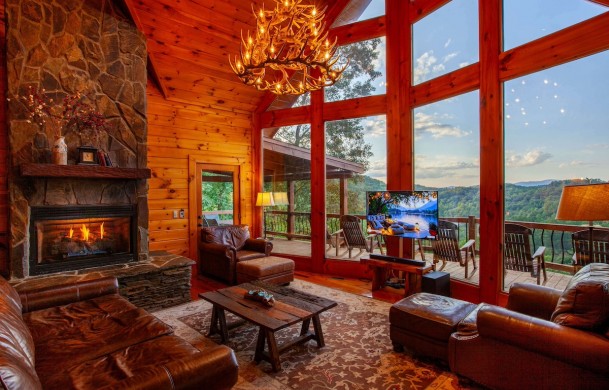 Riverview Lodge | Cabin Rentals of Georgia | Spacious Living Area with two story open ceiling, antler chandelier, leather furnishings, stone gas log fireplace