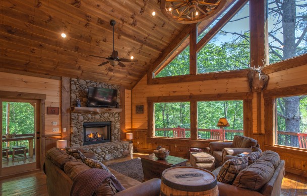 Bright and Welcoming Living Area featuring Stone Gas Fireplace, and SMART TV Aska Escape Lodge | Blue Ridge Cabins | Cabin Rentals of Georgia | Luxury Living Area with cathedral ceilings and large wall of windows capturing beautiful wooded views of North GA